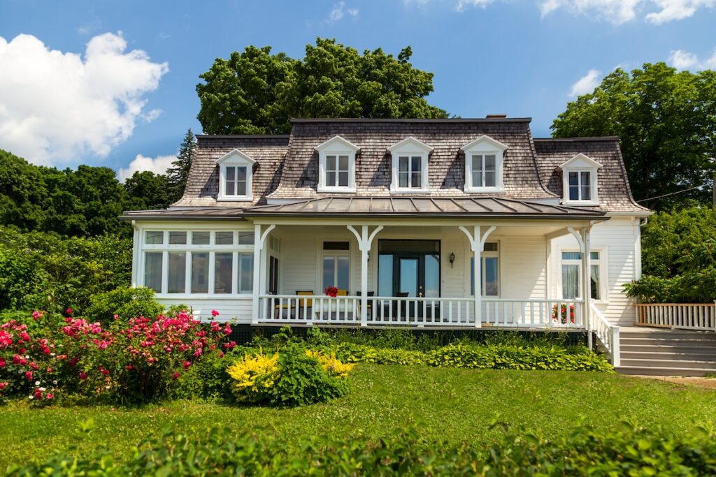 Asymmetrical Second Empire style white country cottage with steeply-pitched mansard roof, seen during a sunny summer day