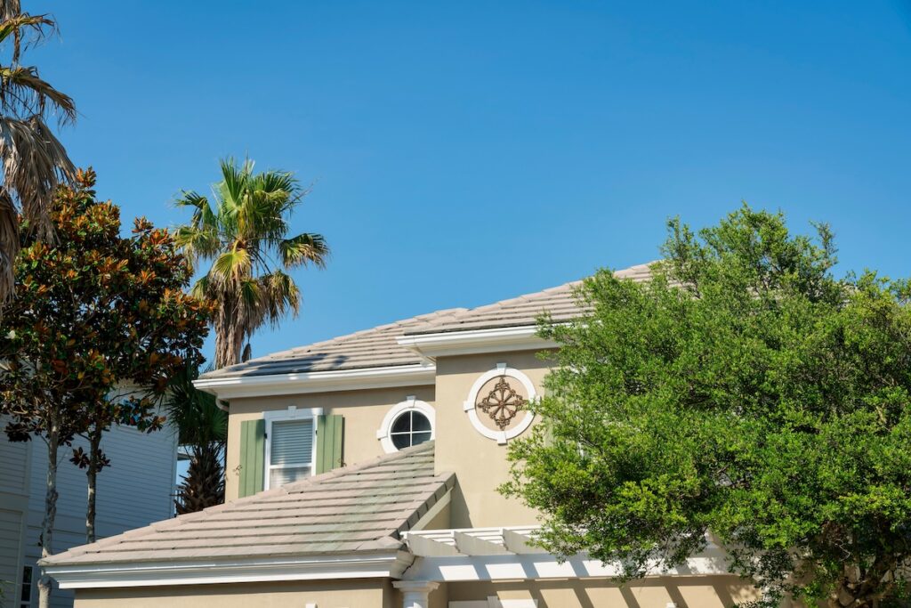 Top exterior of a house with asphalt composite roof shingles at Destin, Florida. There are trees outside the house with round trims with decorative panels and windows and a window with fake shutters.