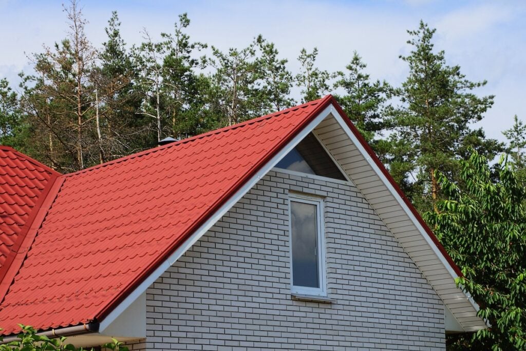 metal roof colors gray brick attic with a window under a red tile roof against the sky and pine trees