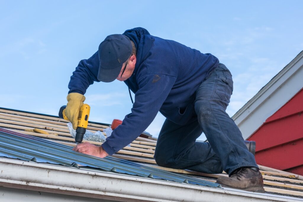 A man working on screwing in a tin roof on a house roof leak repair