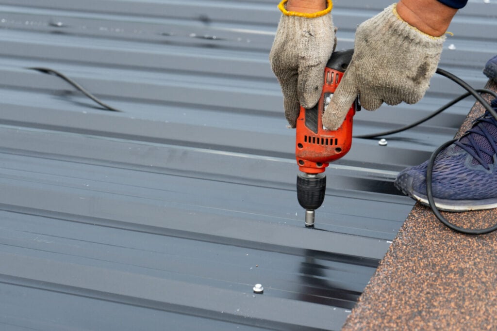 Workers installing the metal sheet roof by electrical drilling machine