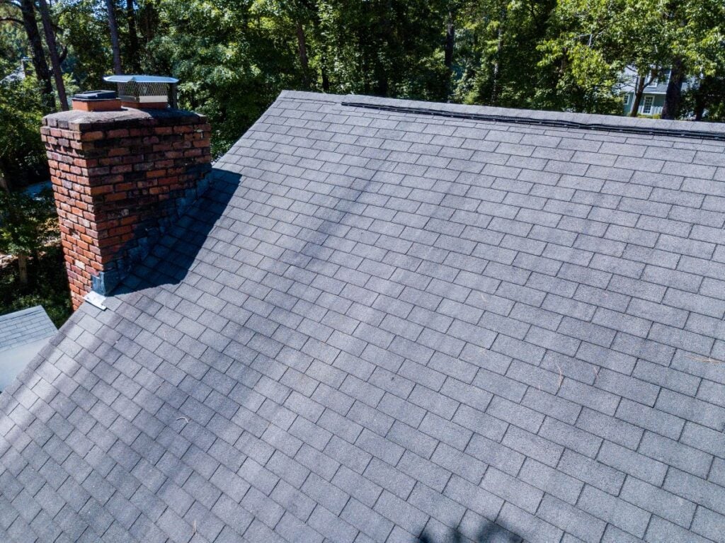 architectural shingles vs 3 tab grey roof brick wall chimney surrounded by trees