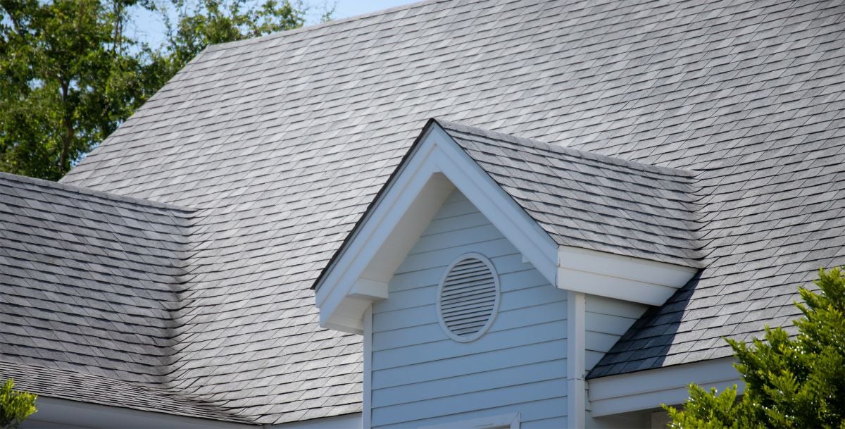 Asphalt shingle roofing on a modern house, showcasing a grey roof with a prominent gable and vent, surrounded by greenery, relevant to residential roofing options and costs.
